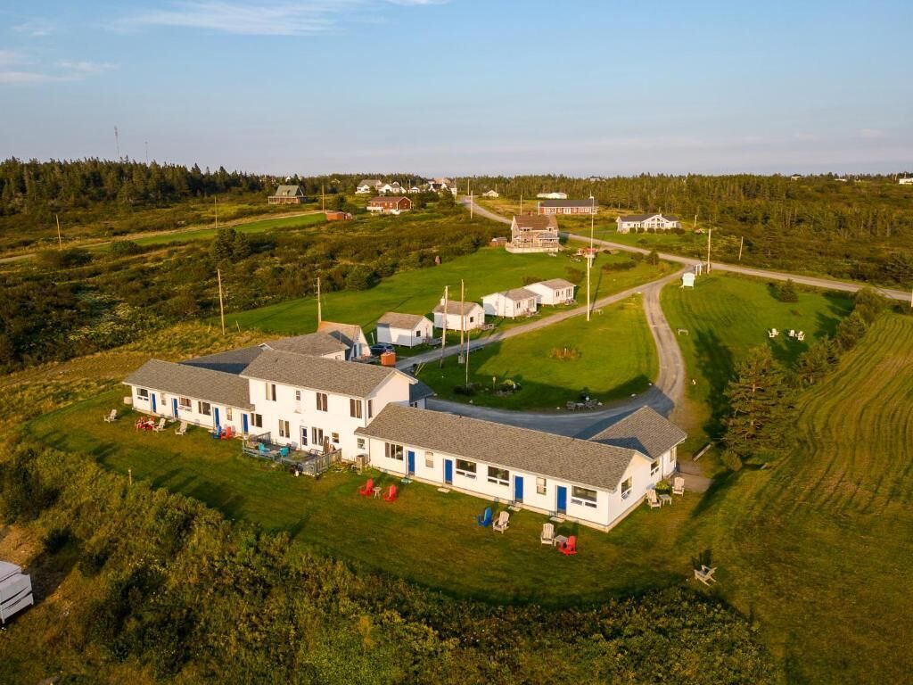 A large white building with multiple rooms, surrounded by green fields and a few smaller structures.