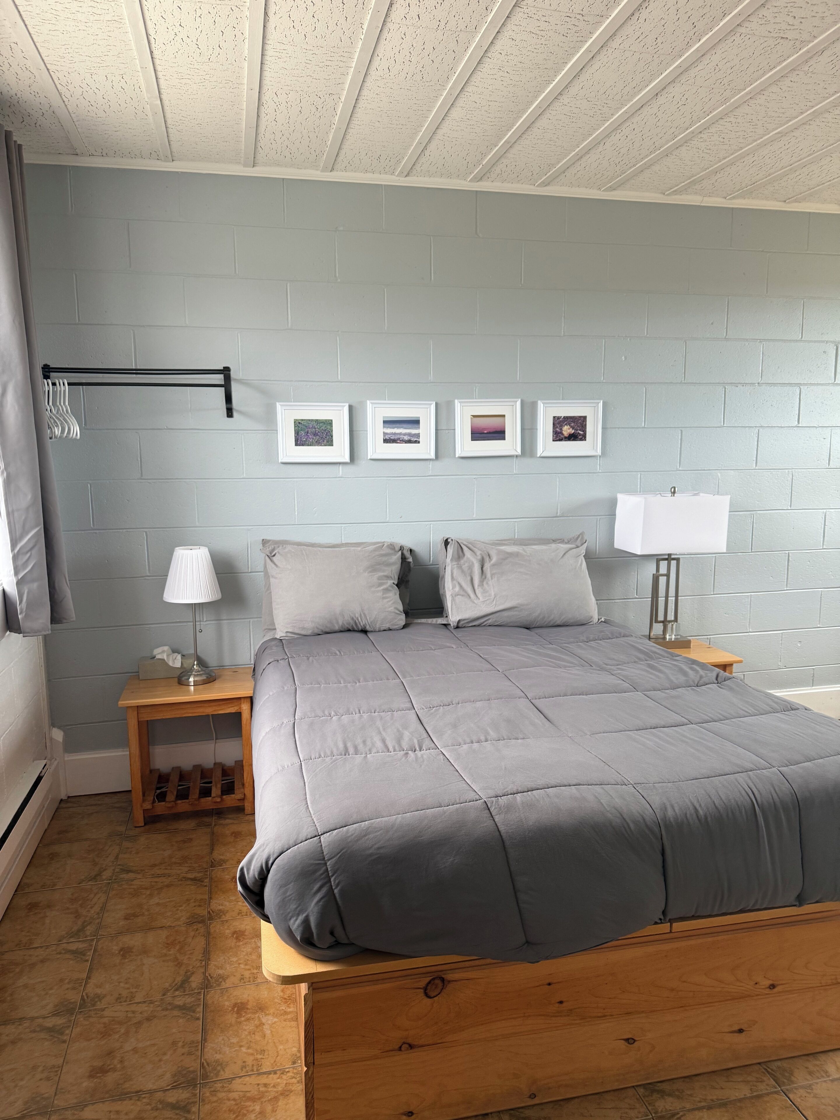 Un dormitorio con una cama, dos mesitas de noche, una lámpara de pared y cuatro cuadros enmarcados.
