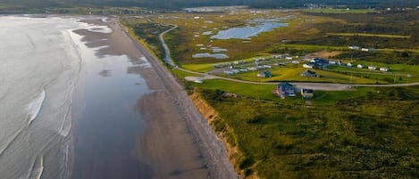 An aerial view of a coastal area with a beach, grassy fields, and several buildings.