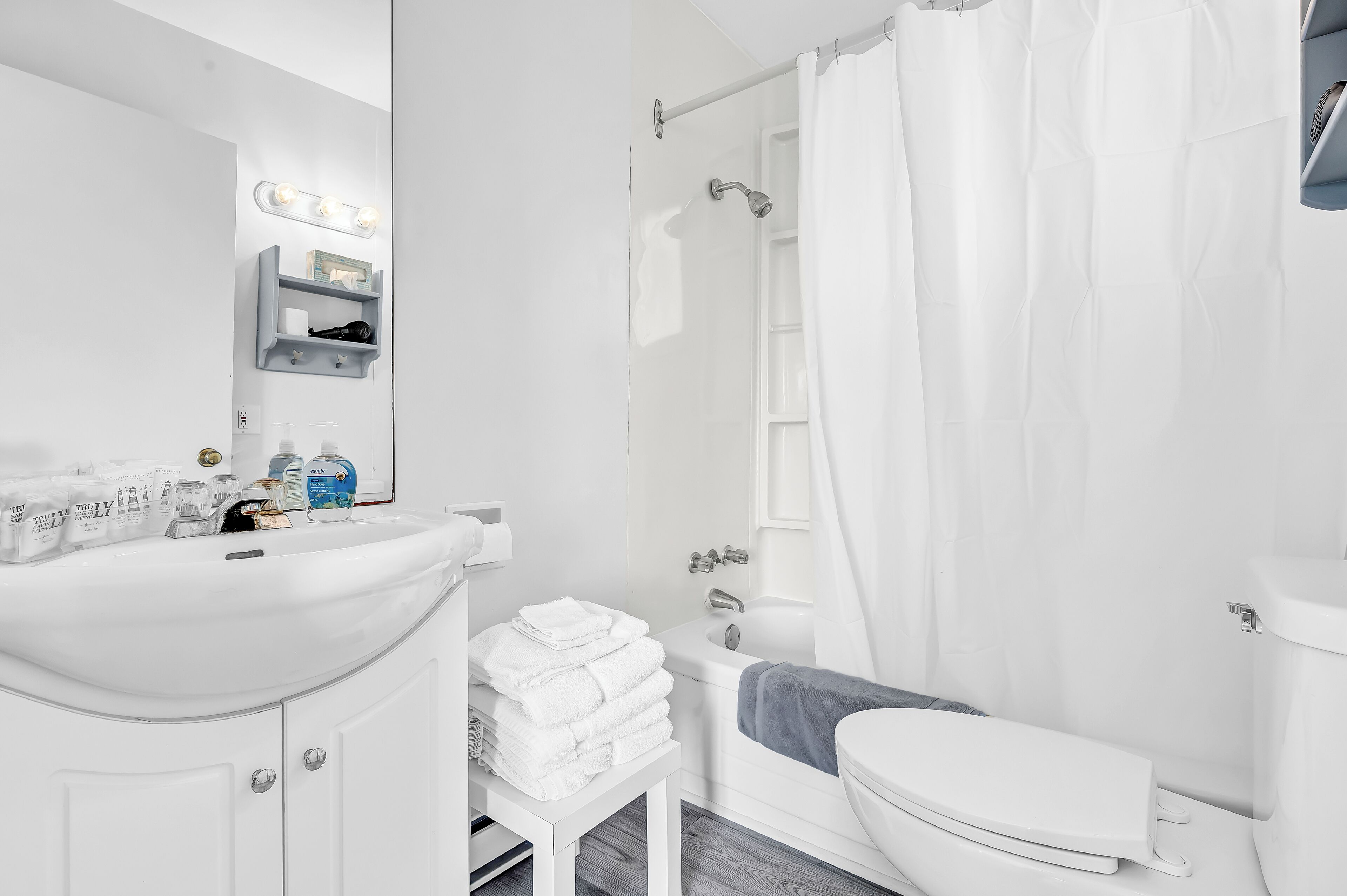Un baño moderno con lavamanos, espejo y tocador blancos, una ducha con cortina y un inodoro.