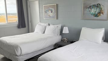 Habitación de hotel con dos camas, una ventana con cortinas, una puerta y dos obras de arte colgadas en la pared.