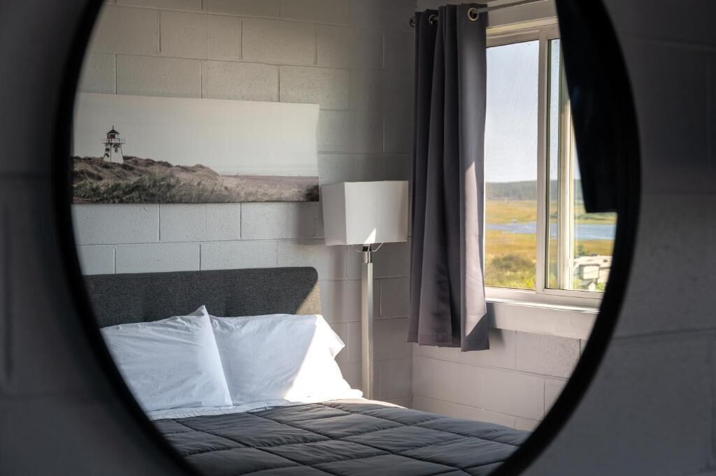 A bedroom with a bed, a nightstand, a lamp, and a view of a lighthouse through a window.
