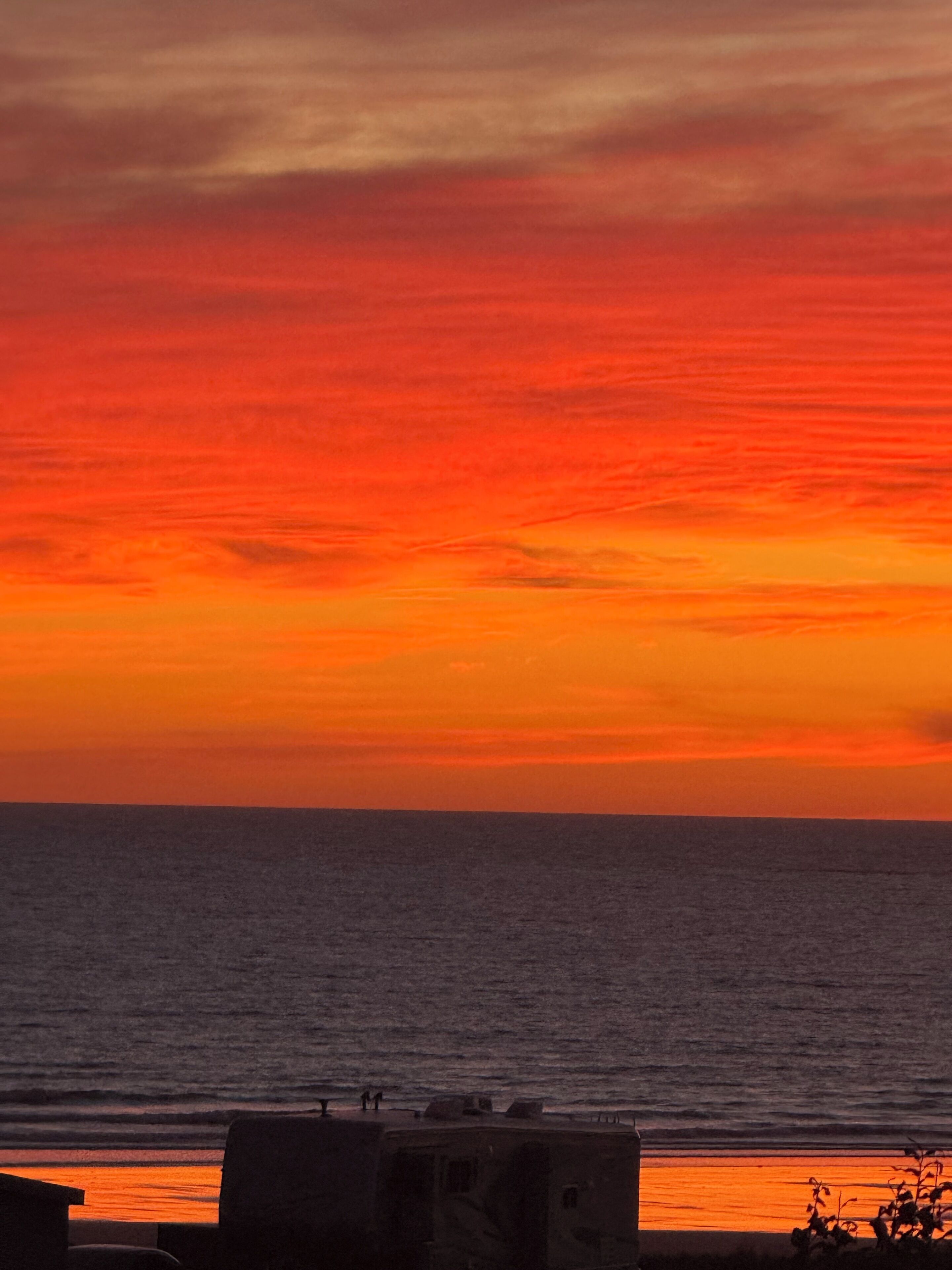 A sunset over the ocean with a view of the sea and a distant shoreline.