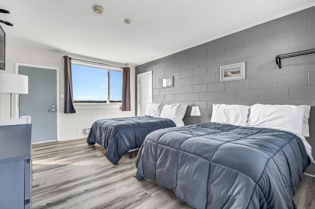 A bedroom with two beds, a window, and a grey brick wall.