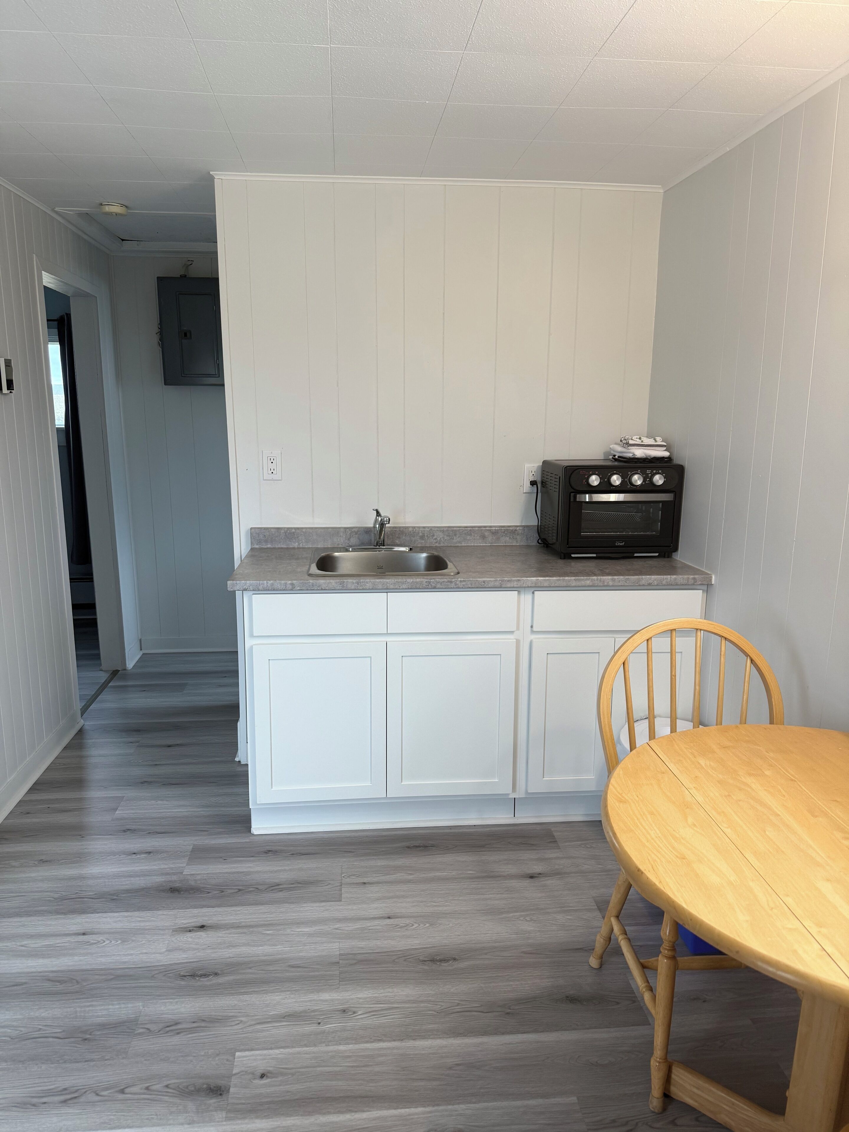 A compact kitchen with white cabinets, a built-in oven, and a wooden dining table.