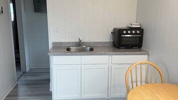 A compact kitchen with white cabinets, a built-in oven, and a wooden dining table.