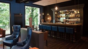 A bar area with a wooden counter, blue bar stools, and a variety of bottles and glasses. - Parkhotel Schillerhain (Kirchheimbolanden)