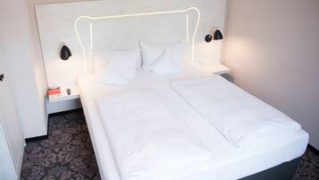 Un lit bien fait, avec du linge de lit blanc, une tête de lit dotée d’un éclairage intégré et des lampes de chevet.