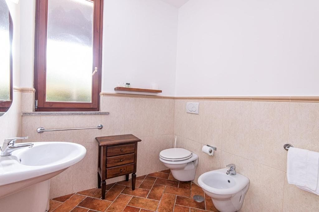 A small bathroom with a sink, toilet, bidet, and a wooden cabinet.