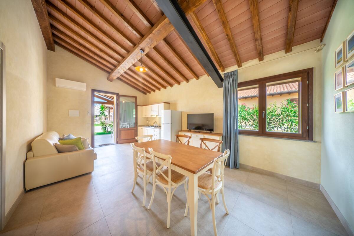 A spacious living area with a wooden dining table and chairs, a sofa, and a TV.
