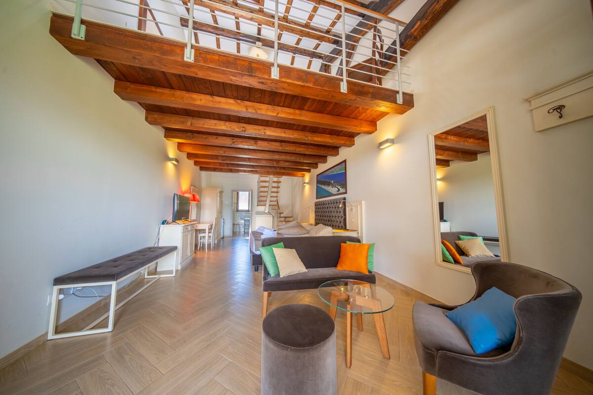 A spacious living area with a high wooden ceiling, a sofa with colorful cushions, a glass coffee table, and a bench.