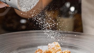 Eine Person bestreut ein Dessert in einer klaren Glasschale mit Puderzucker.