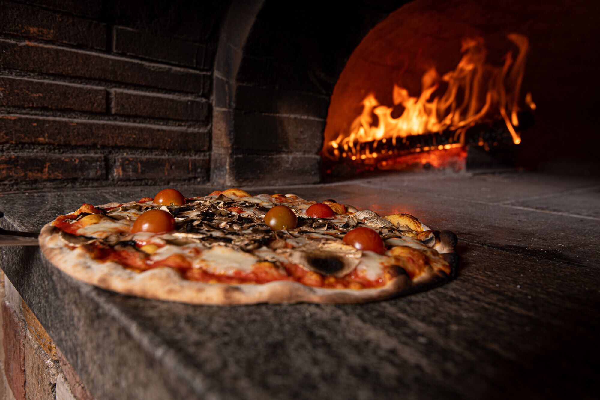 En pizza som bakas i en vedeldad ugn med synliga lågor.