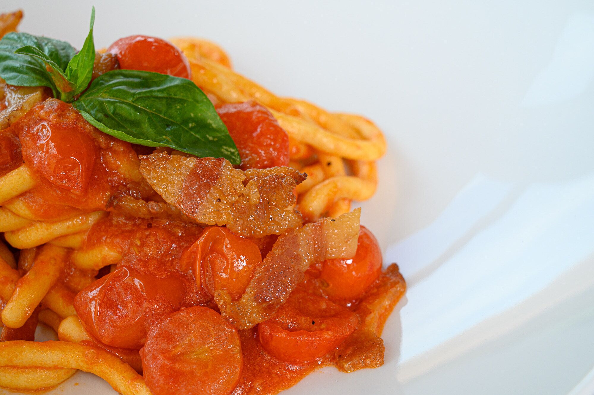 A plate of spaghetti with tomato sauce, bacon, and cherry tomatoes.