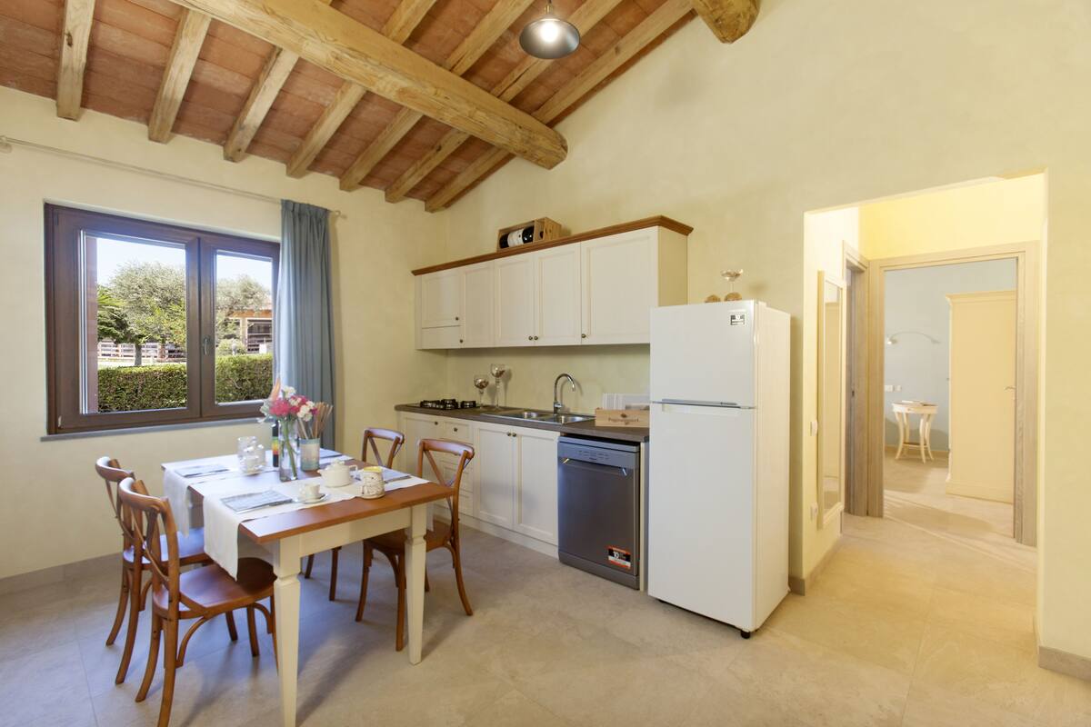 A kitchen with wooden beams, white cabinets, a dishwasher, and a dining area with a table and chairs.