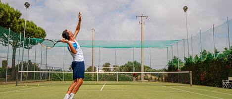 A tennis court with a player in mid-action, a net, and surrounding fencing.