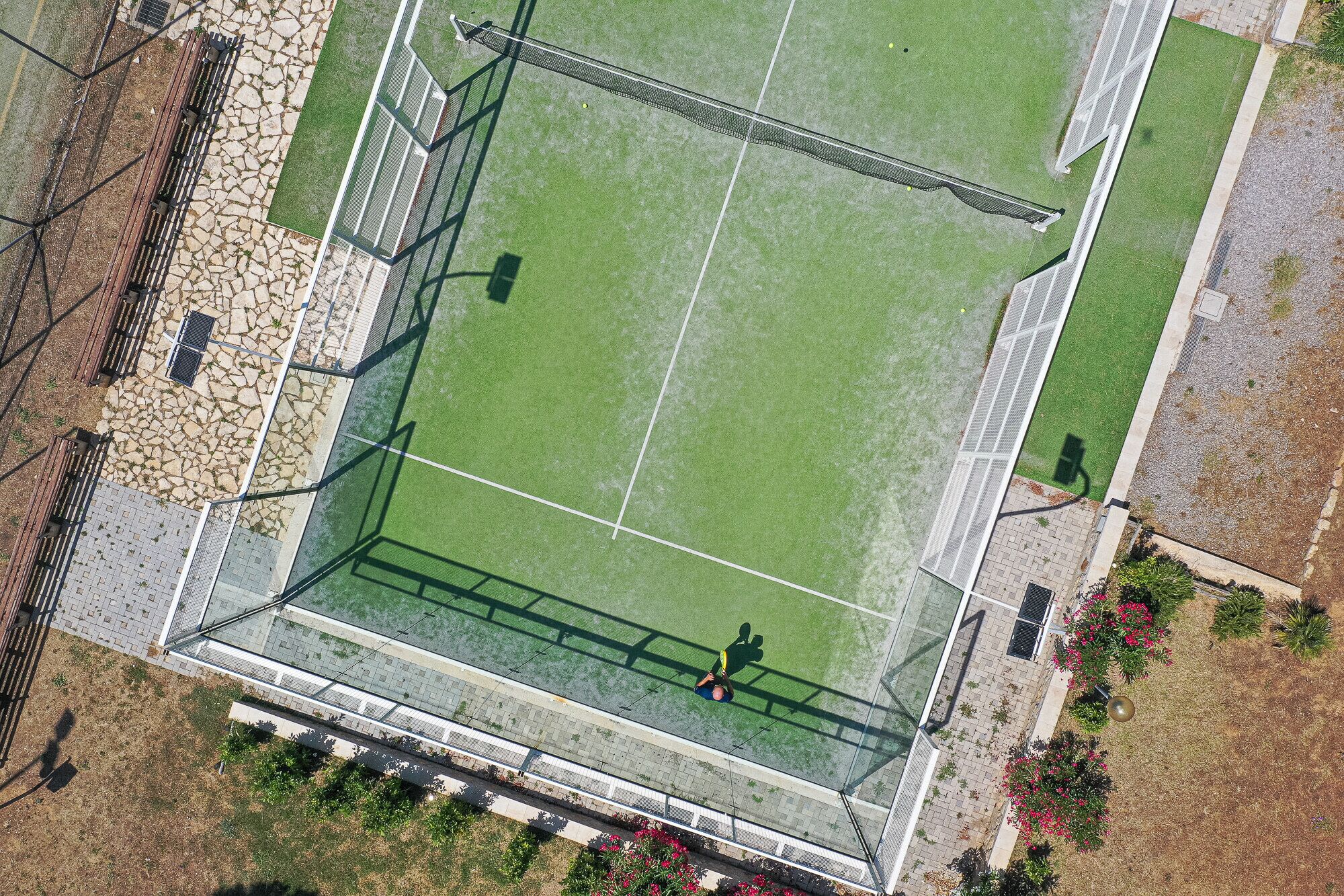 An aerial view of a sports field with a fenced area, spectator stands, and surrounding landscaping.