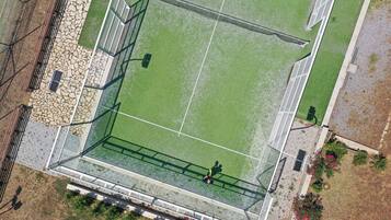 An aerial view of a sports field with a fenced area, spectator stands, and surrounding landscaping.