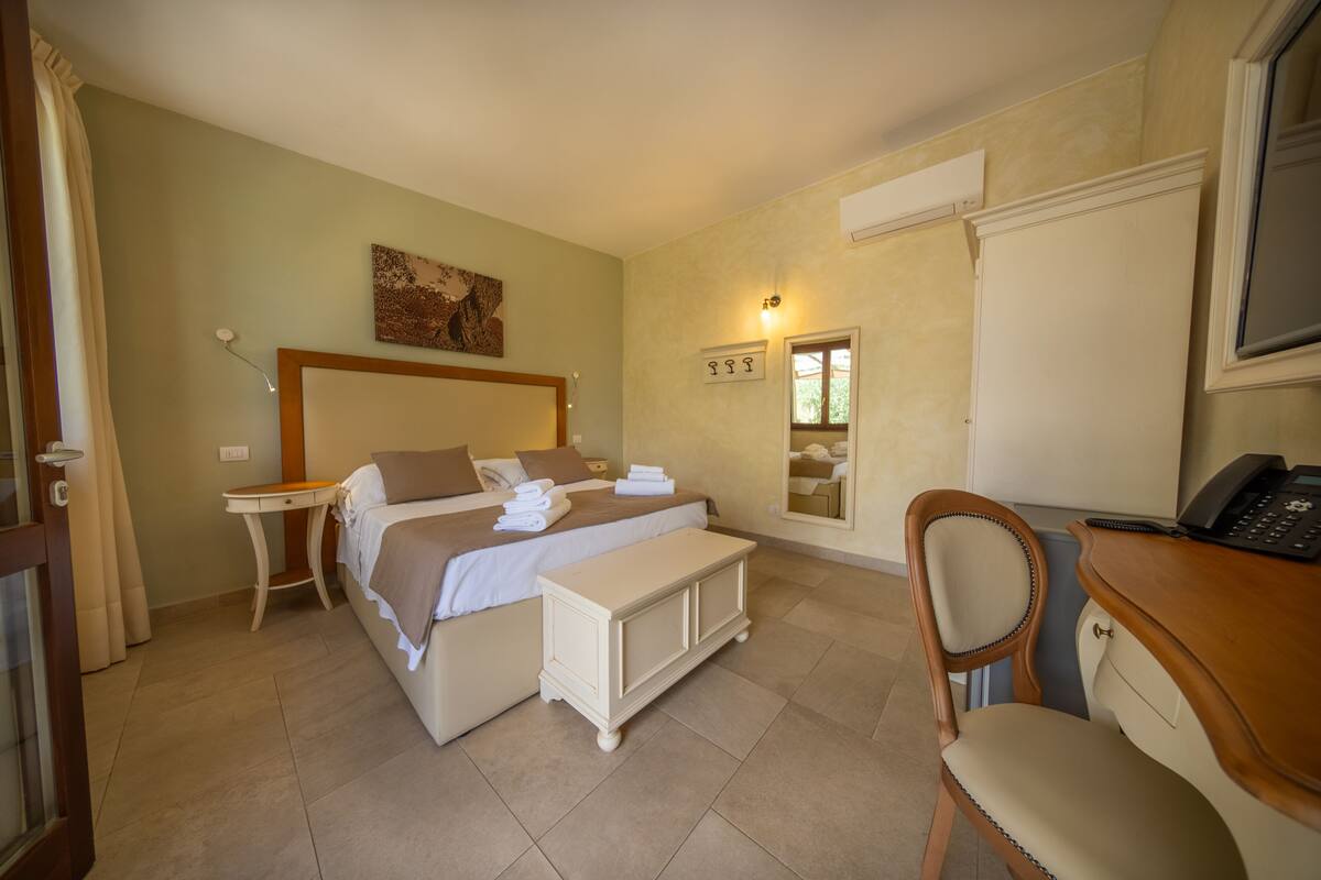 A bedroom with a bed, bedside table, chair, desk, and a mirror.