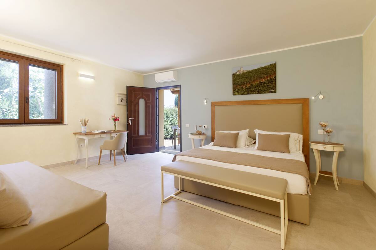 A bedroom with a large bed, a desk, a chair, and a small table with a vase.
