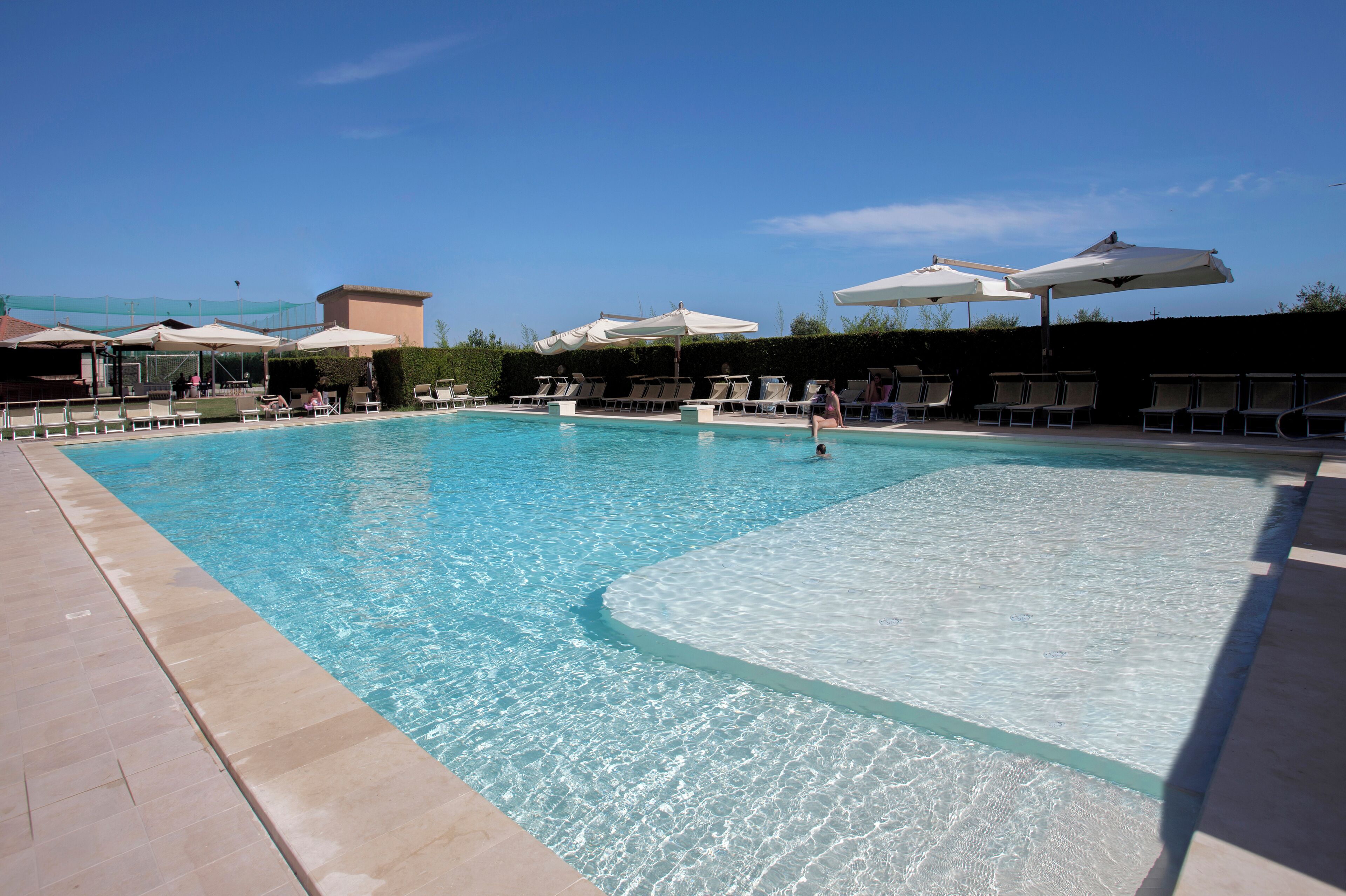 Una piscina cristalina con sillas de descanso y sombrillas, rodeada por un solárium con baldosas.