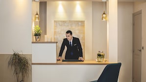 A reception desk with a man in a suit, a potted plant, and a vase of flowers. - Hotel Opera Marigny (Paris)