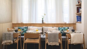 A dining area with a window seat, wooden chairs, a table with a basket of bread, a bowl of fruit, and a vase with flowers. - Hotel Opera Marigny (Paris)