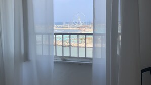 Une chambre avec un lit, une fenêtre ornée de rideaux légers et une vue sur une plage et une grande roue.