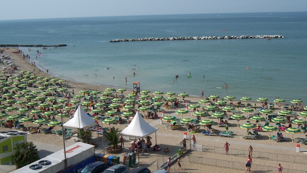 Une plage dotée de nombreux parasols et de chaises longues, d’une digue rocheuse et offrant une vue dégagée sur la mer.