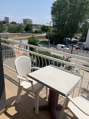 Un balcón con mesa y silla, con vista a un estacionamiento y edificios.