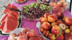 Une table avec différents fruits et une pastèque, un panier et une nappe.