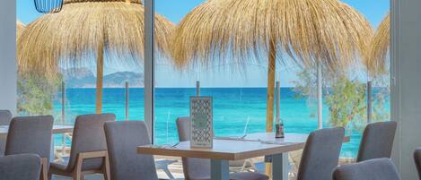 A restaurant with a view of the ocean, featuring thatched umbrellas and modern chairs.