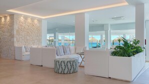 A modern lounge area with white sofas, a patterned ottoman, and a stone wall.