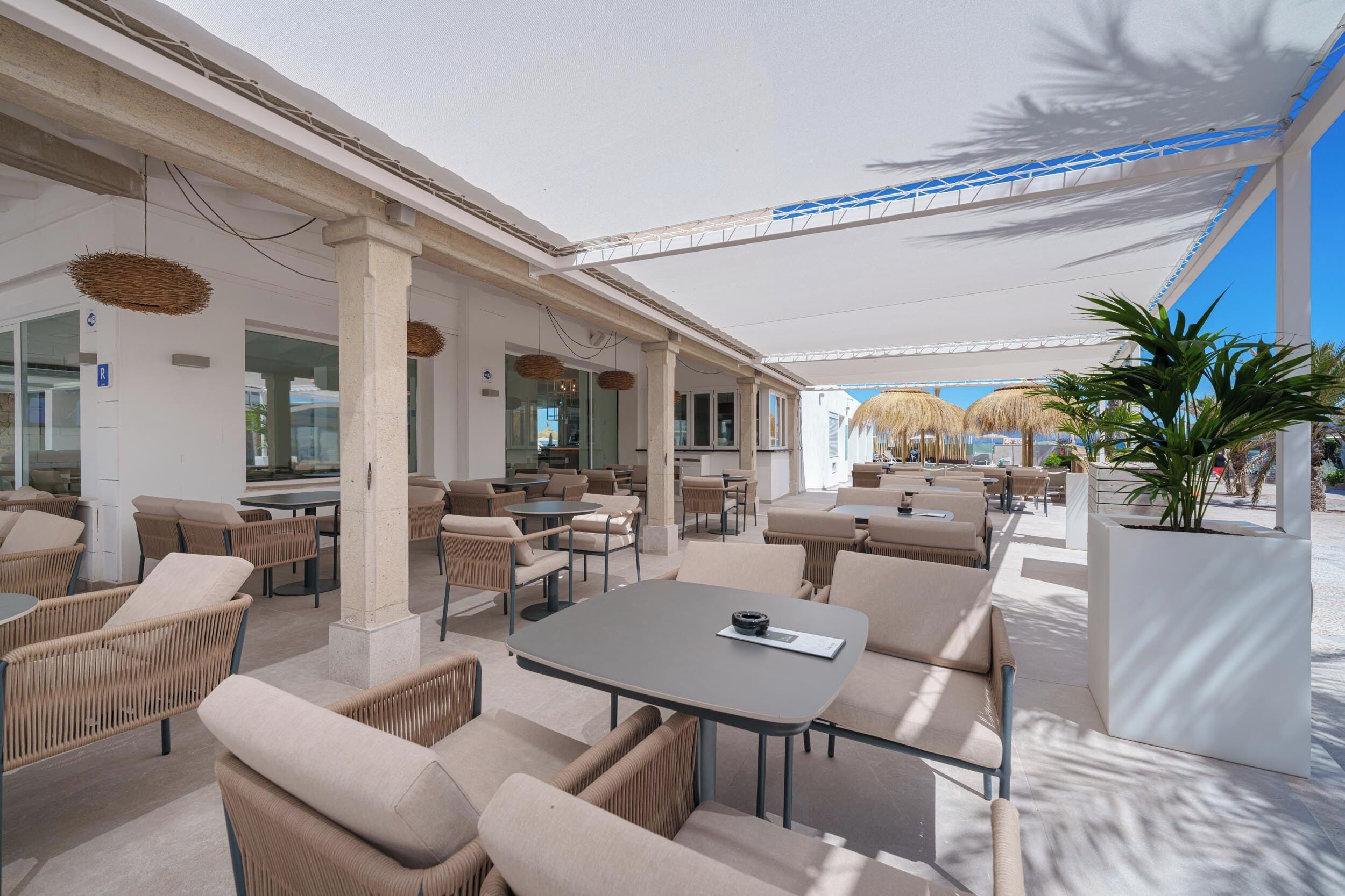 An outdoor seating area with wicker furniture and a large table, shaded by a white canopy.