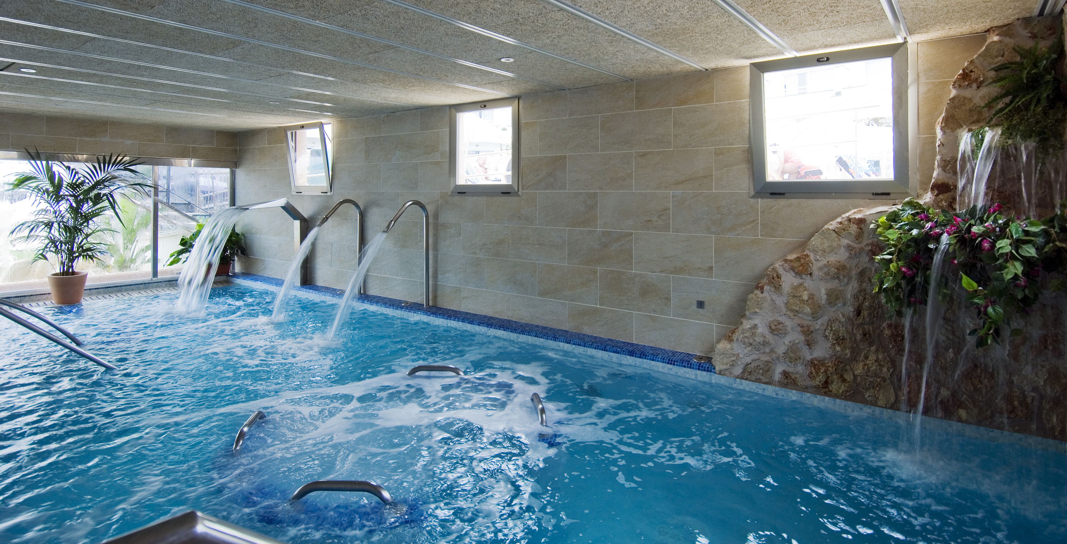 An indoor swimming pool with clear water, built-in steps, and a waterfall feature.