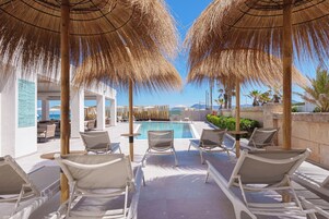 Zona junto a la piscina con sillones de descanso y sombrillas, una piscina y vistas al mar y a las montañas.