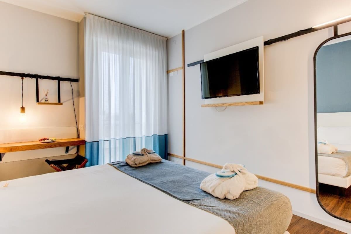 A hotel room with a bed, a desk, a mirror, and a TV.
