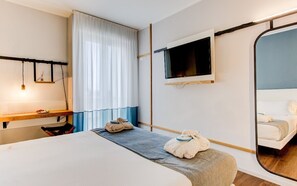 Una habitación de hotel con una cama, un escritorio, un espejo y un televisor.