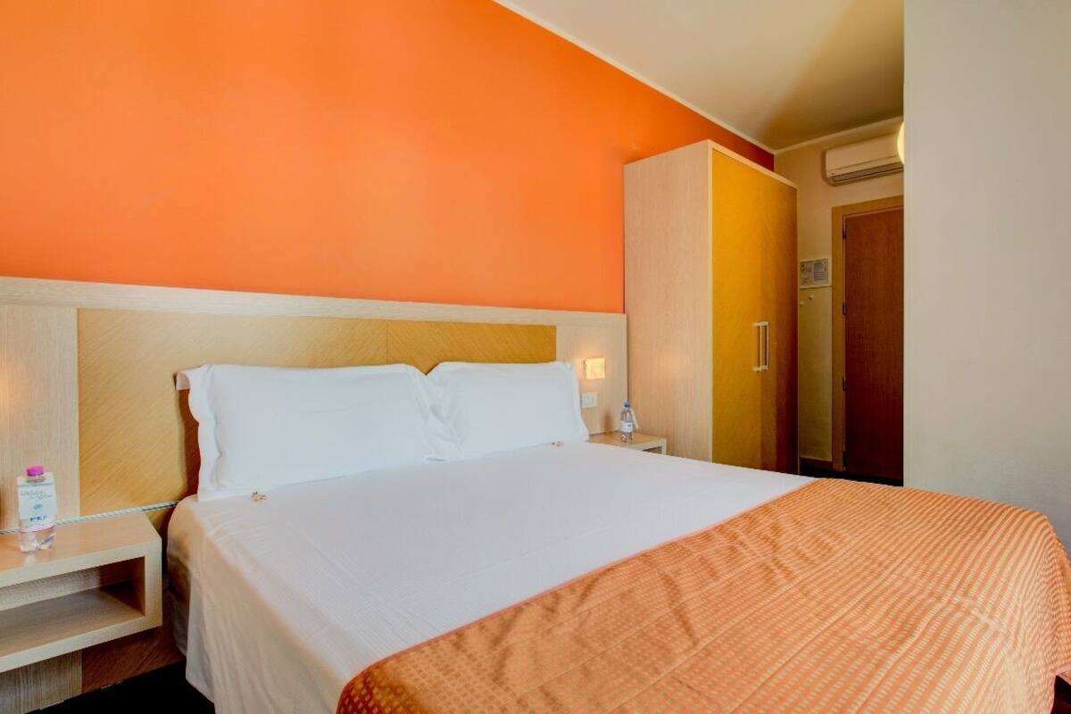 A hotel room with a bed, nightstands, a wardrobe, and an air conditioning unit.
