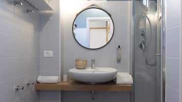 Un bagno con uno specchio tondo, un lavandino bianco, un piano d'appoggio in legno e un box doccia in vetro.