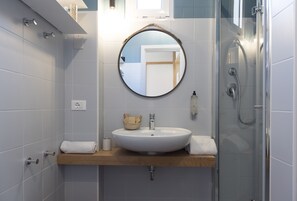 Un baño con espejo redondo, lavamanos blanco, encimera de madera y cabina de ducha de vidrio.