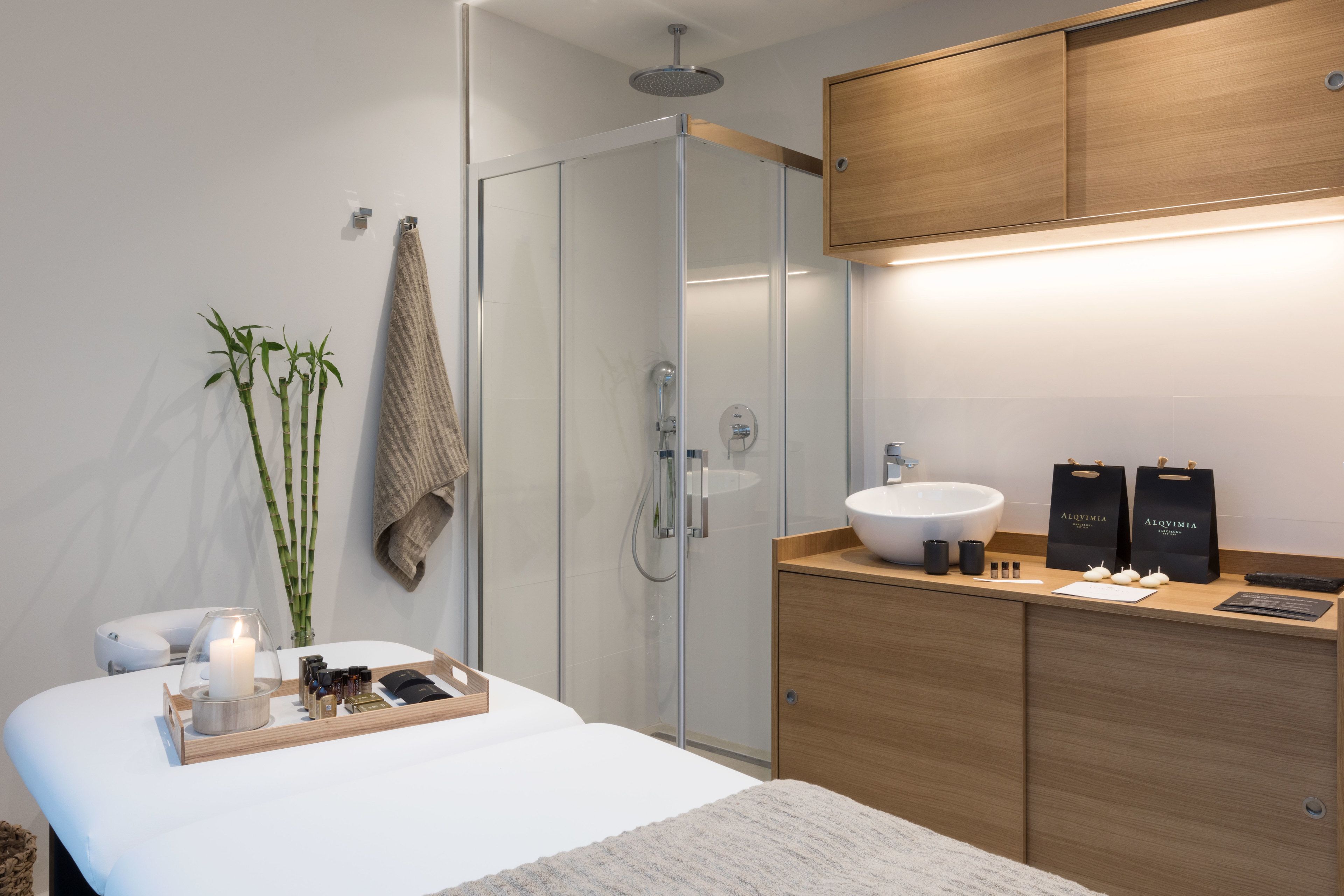 Un baño moderno con cabina de ducha de vidrio, tocador de madera con un lavamanos grande y una bandeja con artículos de aseo.