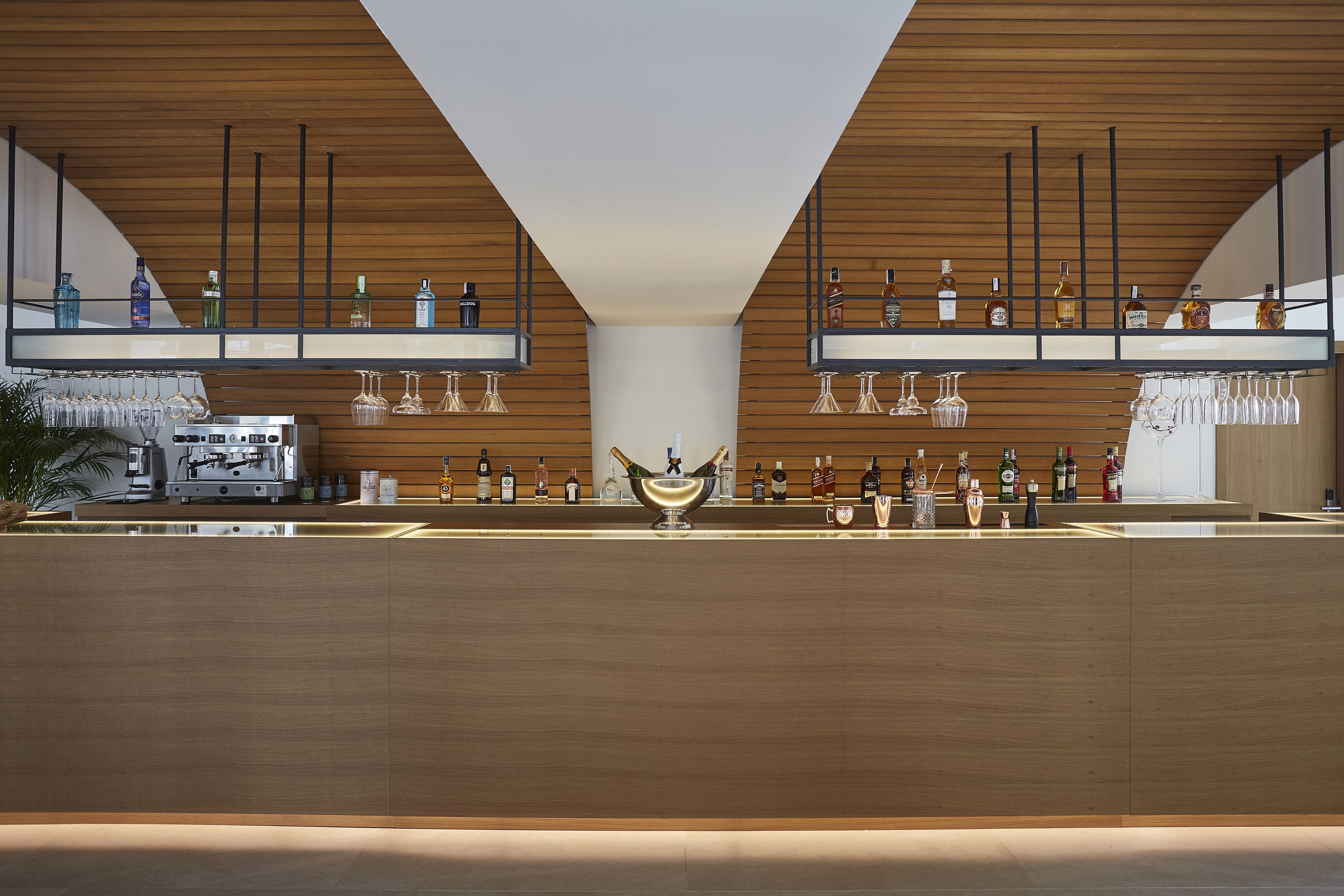 Un bar moderno con paneles de madera, estantes llenos de botellas de licor y copas de vino.