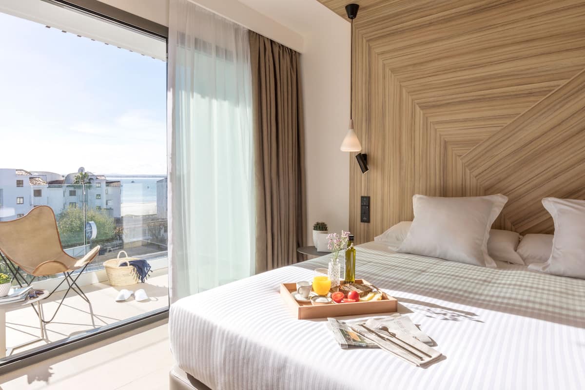 A hotel room with a large window, a bed with a checkered bedspread, a tray of breakfast items, and a view of buildings outside.