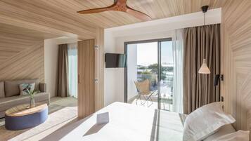 Una habitación de hotel moderna con una cama grande, un televisor de pantalla plana, un ventilador de techo y vistas a la ciudad a través de amplias ventanas.