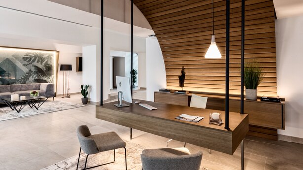 Un área de recepción moderna con un mostrador de madera, dos sillas grises y una lámpara colgante.