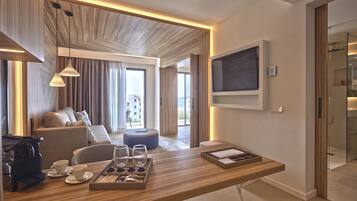 Ein modernes Hotelzimmer mit einem Holztisch, Sitzgelegenheiten, einem an der Wand befestigten Fernseher und Blick auf die Stadt durch das Fenster.