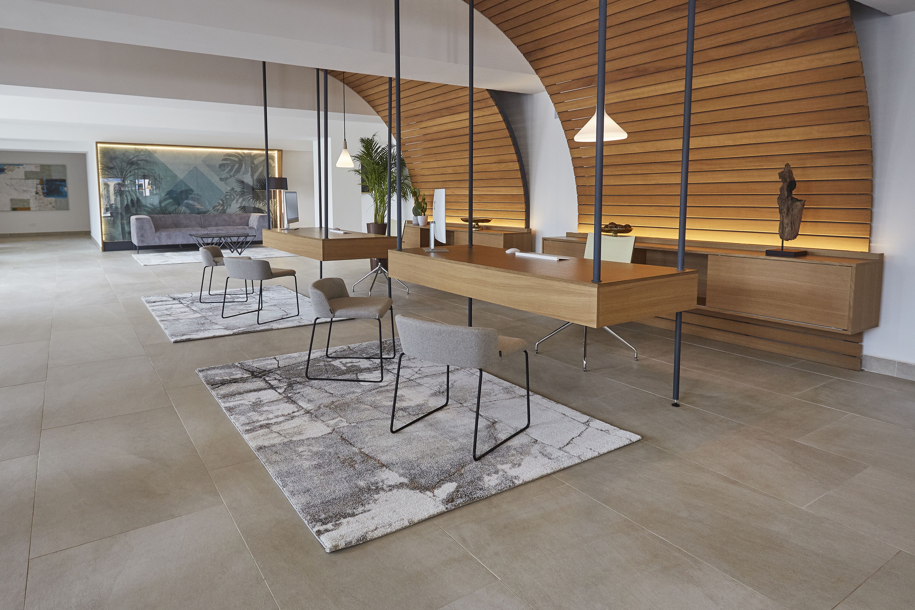 A modern reception area with a wooden reception desk, two grey chairs, a large rug, and a plant.