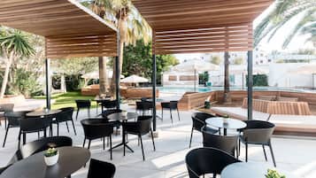 An outdoor patio area with tables and chairs, a pool, and palm trees.