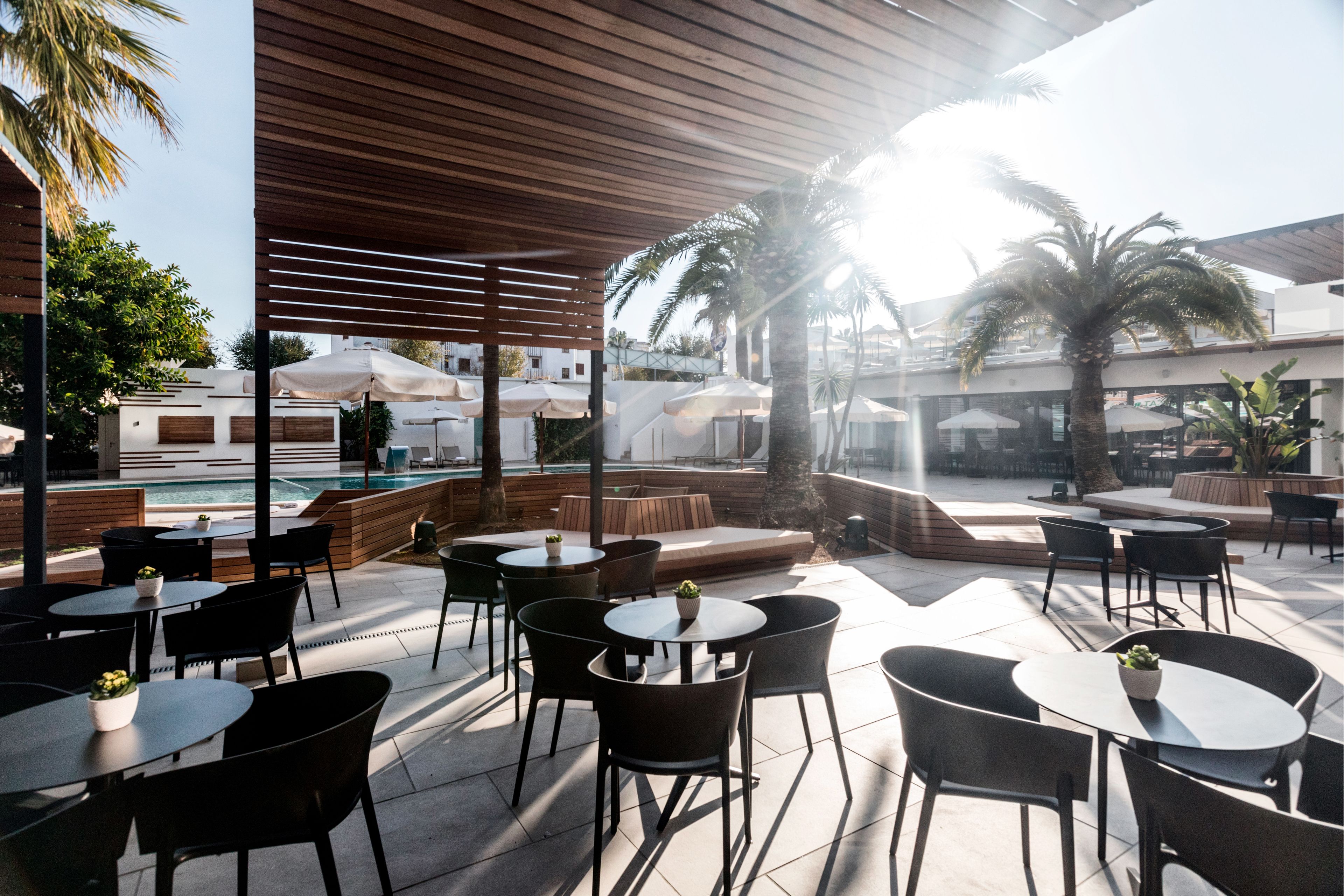 An outdoor patio area with round tables and chairs, a pool, and palm trees.